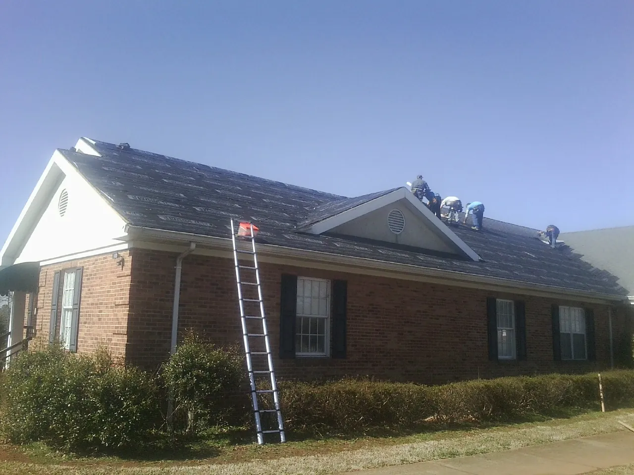 Crew tearing shingles off a brick ranch roof with a ladder set — Metal Roof Repair work by our crew in Plainfield